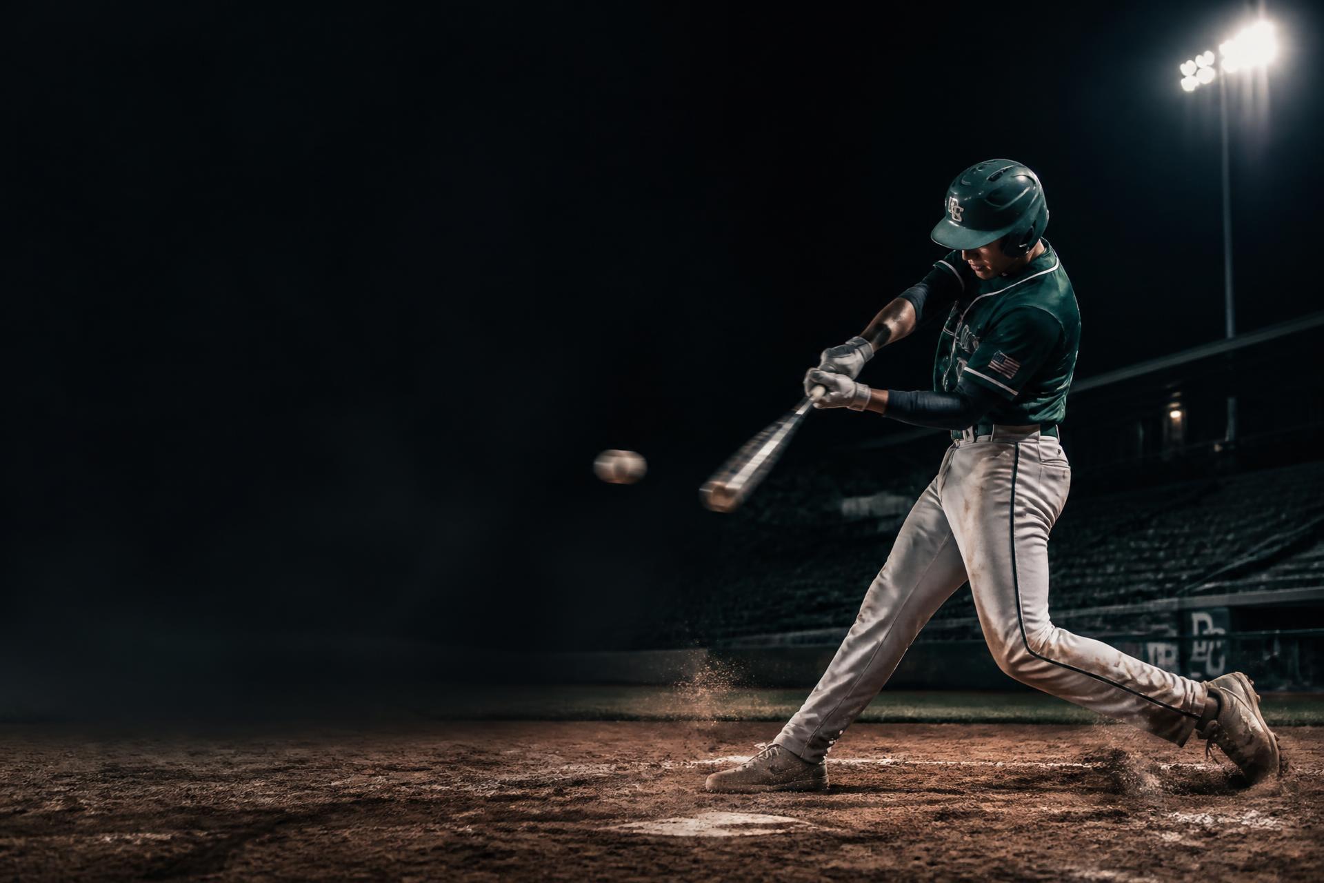 Varsity baseball player mid-swing under stadium lights